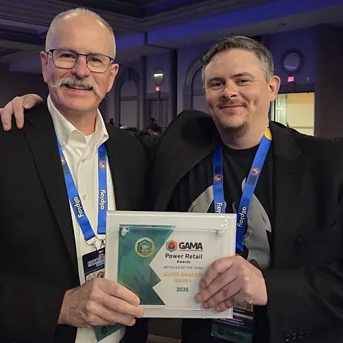 Mike DeBoard and his father holding GAMA's 2026 Retailer of the Year award for Silver Dragon Games